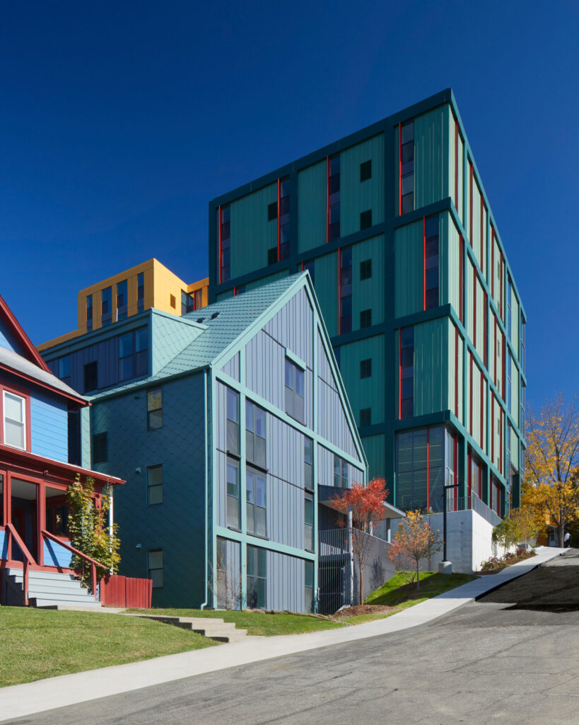 Street-level view of metal-clad buildings in Ithaca’s Collegetown, showing varied heights and vivid facade colors.