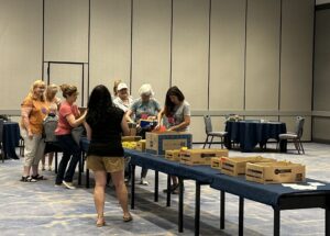 FGIA Fall Conference attendees stand at a table filling backpacks for underprivileged children. 