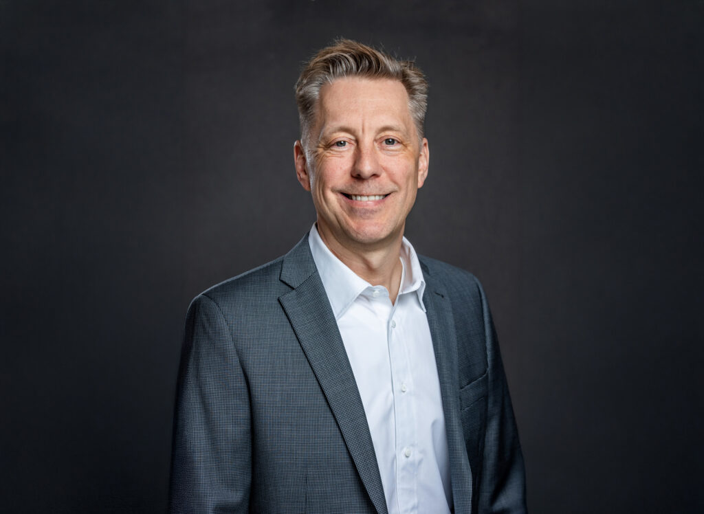 Professional headshot of Troy Johnson in grey suit jacket and white shirt