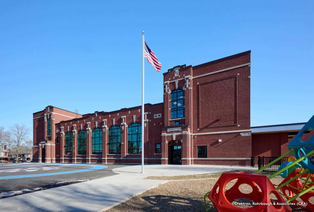 Exterior of Steele Elementary School showing restored brick facade, large windows, and a flagpole in front of the entrance.