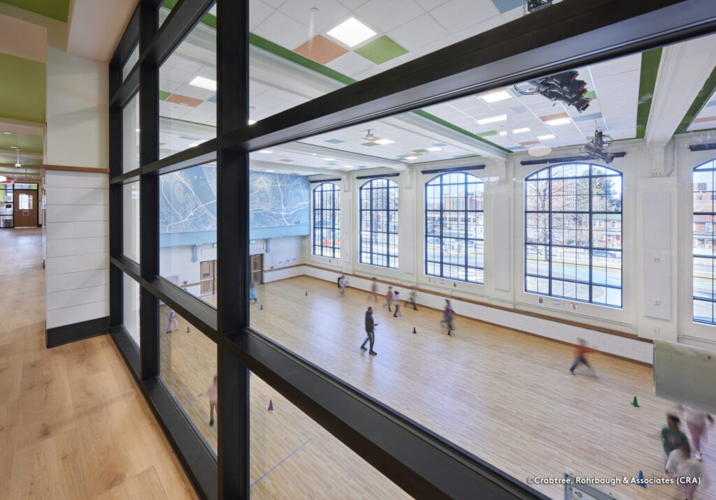 Interior view of Steele Elementary gymnasium with large multi-pane windows and students playing on the court.