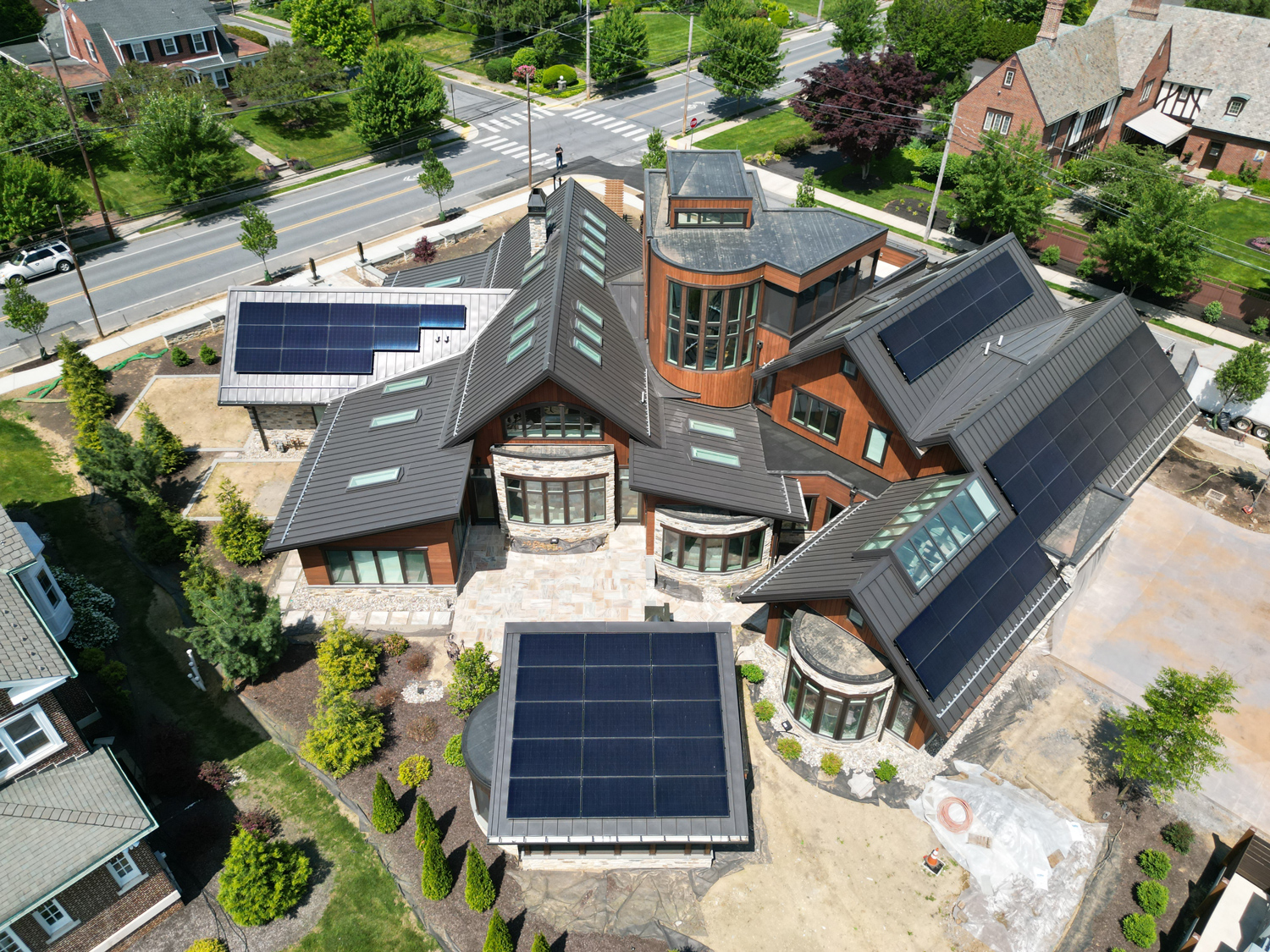 Aerial view of a large contemporary home with intersecting rooflines, clad in standing seam metal and topped with solar panels.