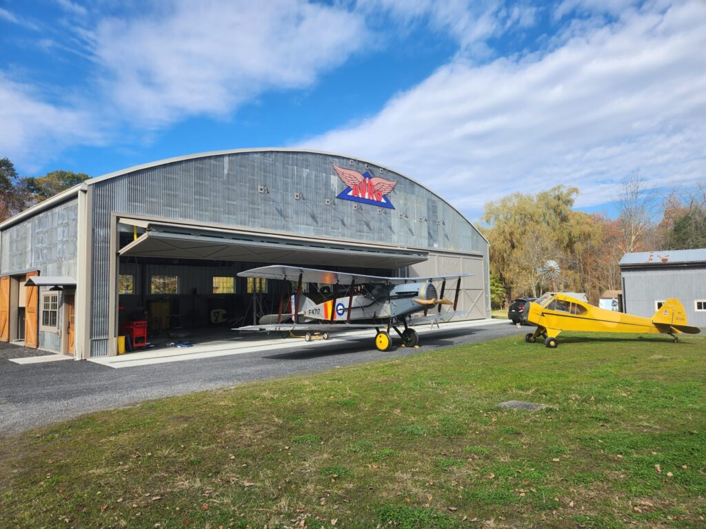 A vintage yellow biplane is parked in front of a hangar marked "Roosevelt Field School of Aviation."