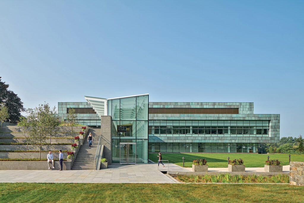 Modern glass and copper-clad expansion building at New England Biolabs in Ipswich, Mass., surrounded by landscaped green space.