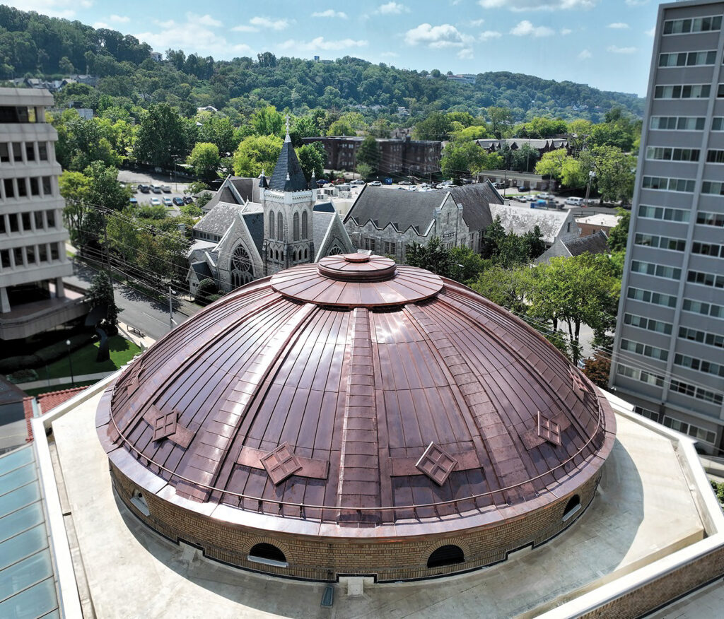 A restored neoclassical copper dome rises above Temple Emanu-El in Birmingham, Ala., surrounded by city buildings and green hills.