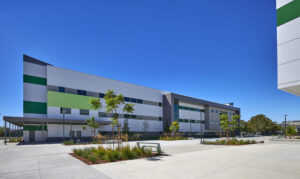 Building exterior facade with panels. Colored in greyscale, except for central left exterior panel in lime green. Palm trees and other foliage are visible in the landscaping.