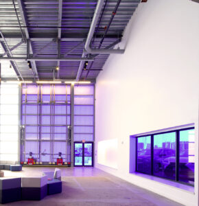 Interior of the ICA Watershed with exposed steel ceiling, large translucent bifold door, and purple lighting reflecting on gallery walls.