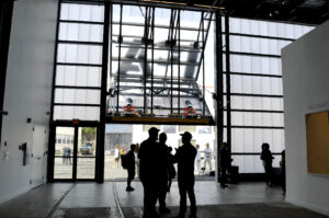Visitors stand inside the ICA Watershed near a large translucent bifold door opening outward, creating a bright entryway framed by polycarbonate panels.