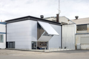 Exterior view of the ICA Watershed with a translucent polycarbonate bifold door partially open, contrasting the surrounding industrial buildings.