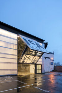 ICA Watershed bifold door partially open at dusk, with translucent polycarbonate panels glowing from interior light and logo visible across the facade.