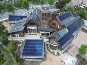 Overhead view of home with solar panels and metal roofing visible. Foliage off to the side. Photograph taken during the daytime.