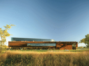 Distant exterior view of the large, wide structure, photographed in front of a yellow field.