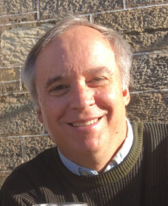 Headshot of Christopher Hoskins in knit sweater with shirt collar. Photographed outdoors.