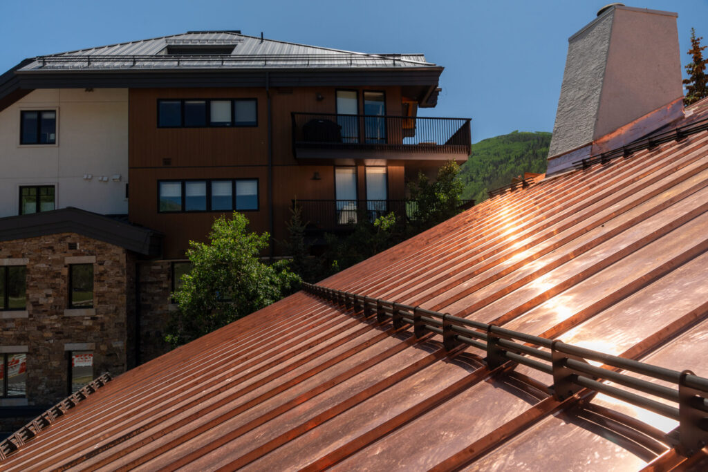 Showcasing metal roofing snow retention is a shining copper-colored roof with reflective natural light visible. Small snow fence installed across the metal panels.