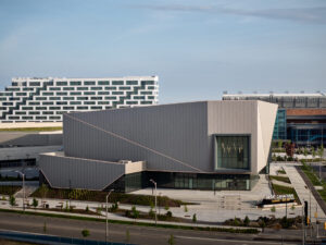Exterior view of large geometric building featuring grand grey metal panels as cladding.