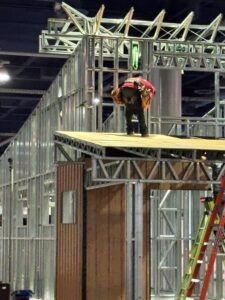 Steel framing of a structure with wood appearance of panels. Man stands on scaffolding.