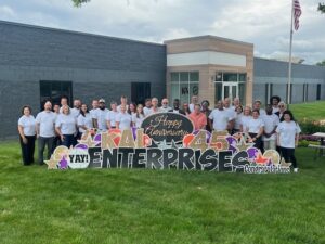 This photo captures the KAI Enterprises St. Louis team, a group of over 15 people gathered on green grass during the daytime.