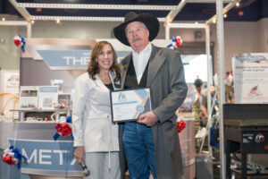 Two people stand indoors posed for a picture. One holds a certificate.