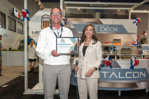 Two people stand indoors, smiling. One holds a certificate.