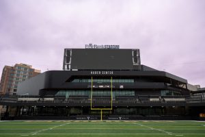 A view of the building that includes a green field and yellow goal post in front of the black structure.