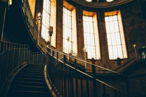 Metal railing and staircase in the interior of a dimly daylit building.