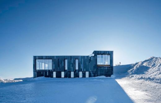 Rectangular kirigami-inspired home with black and grey cladding on a snowy hill.