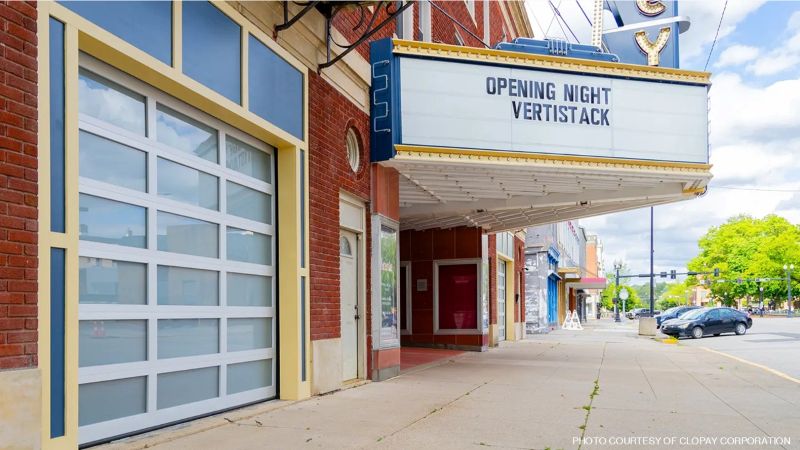 Historic brick theater façade with a modern frosted-glass sectional door beneath a marquee reading “Opening Night Vertistack.”