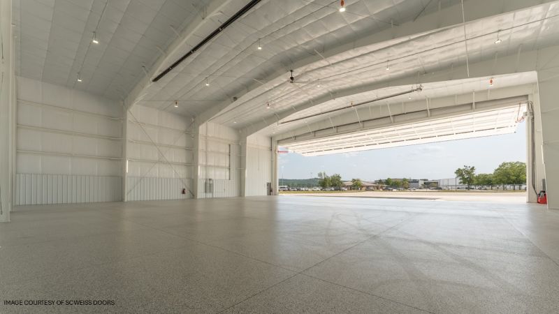 Interior: Spacious white metal aircraft hangar interior with a polished concrete floor and the large door open to the airfield.
